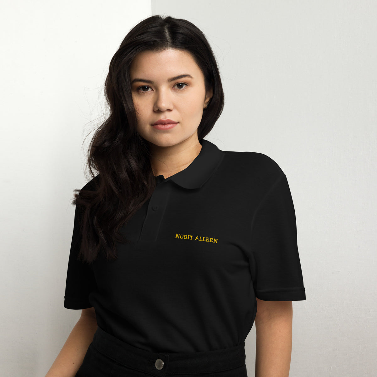 Woman wearing a white Nooit Alleen polo shirt with yellow text.