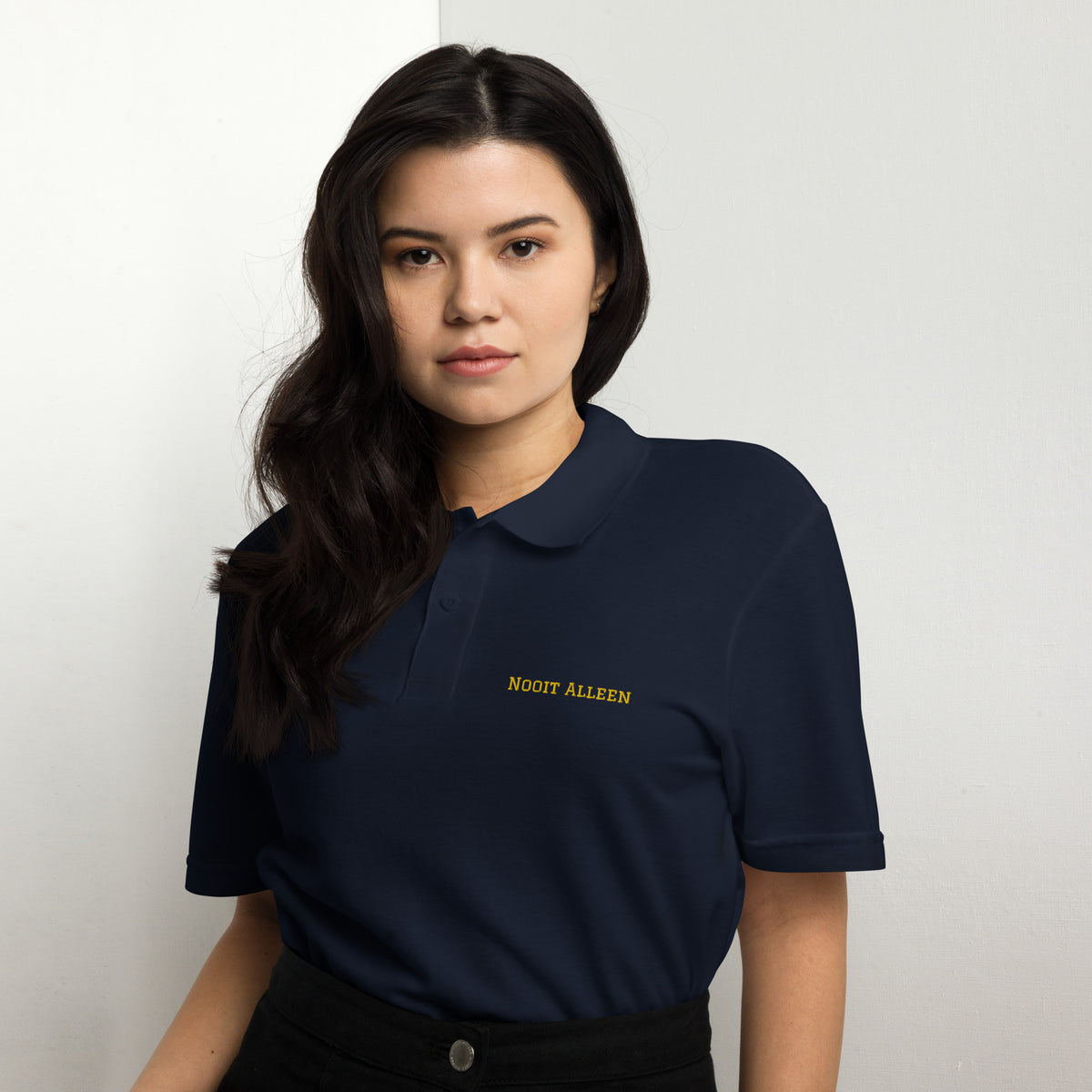 Woman wearing a white Nooit Alleen polo shirt with yellow text.