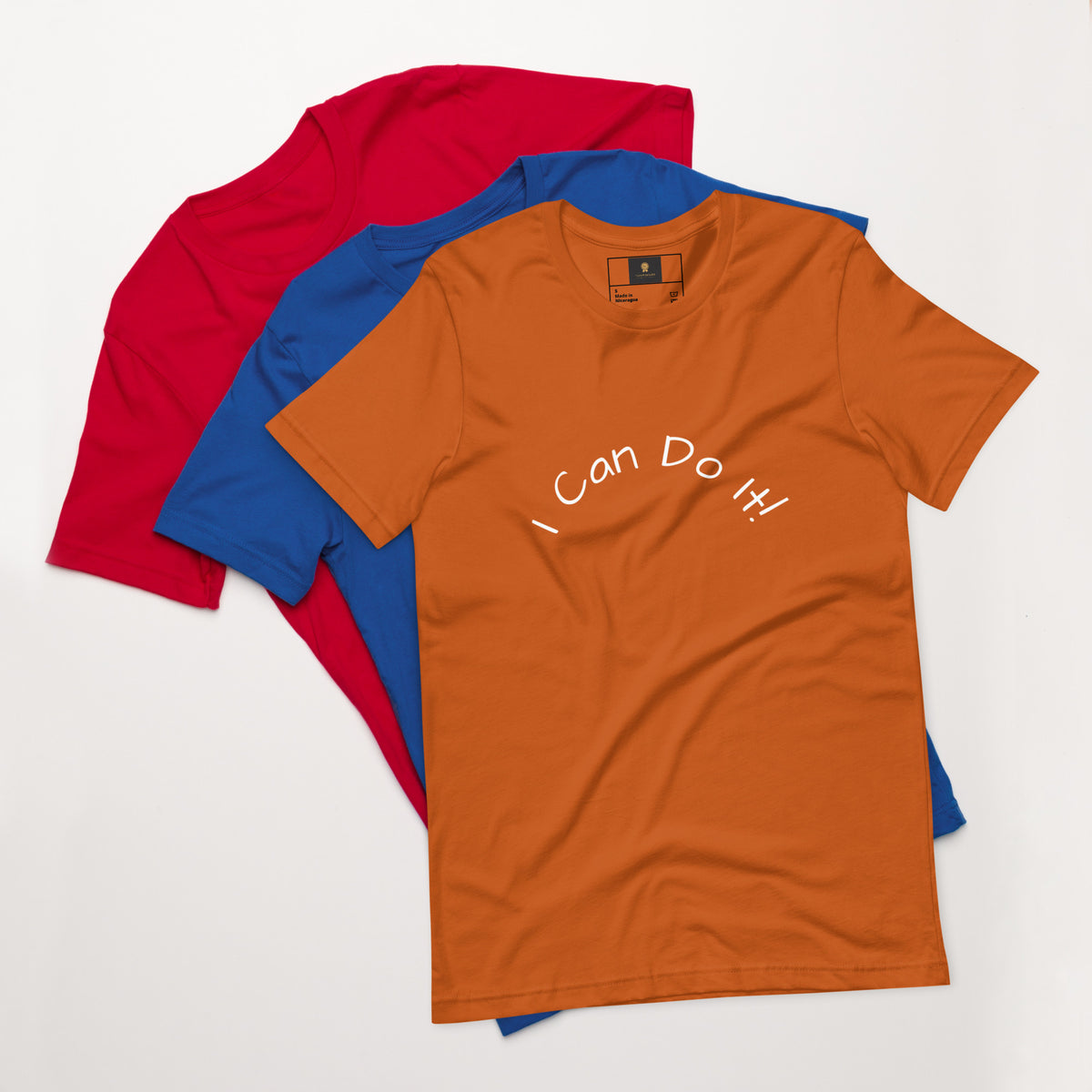 I Can Do It Unisex T-shirt in gray with red and blue shirts stacked in the background.