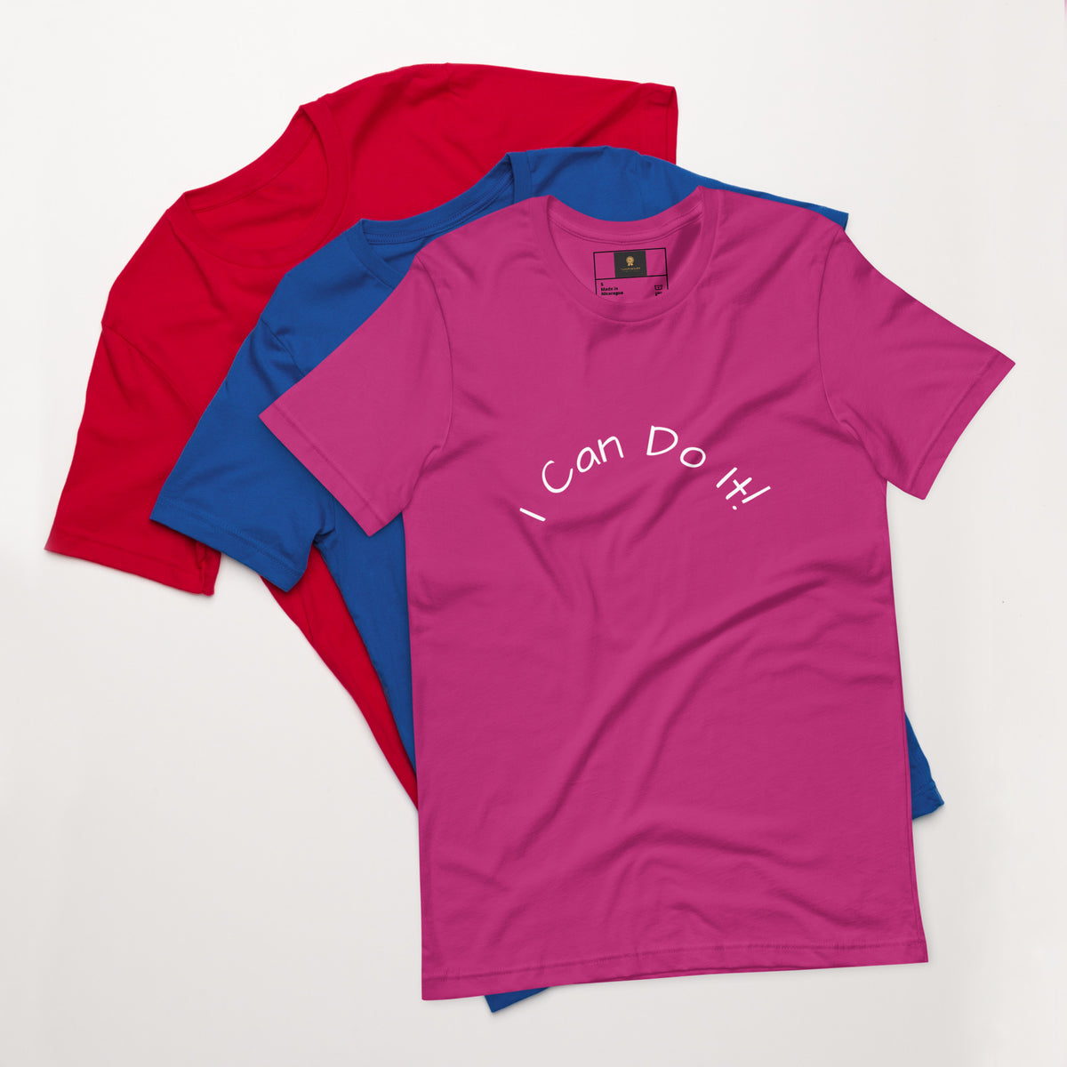 I Can Do It Unisex T-shirt in gray with red and blue shirts stacked in the background.
