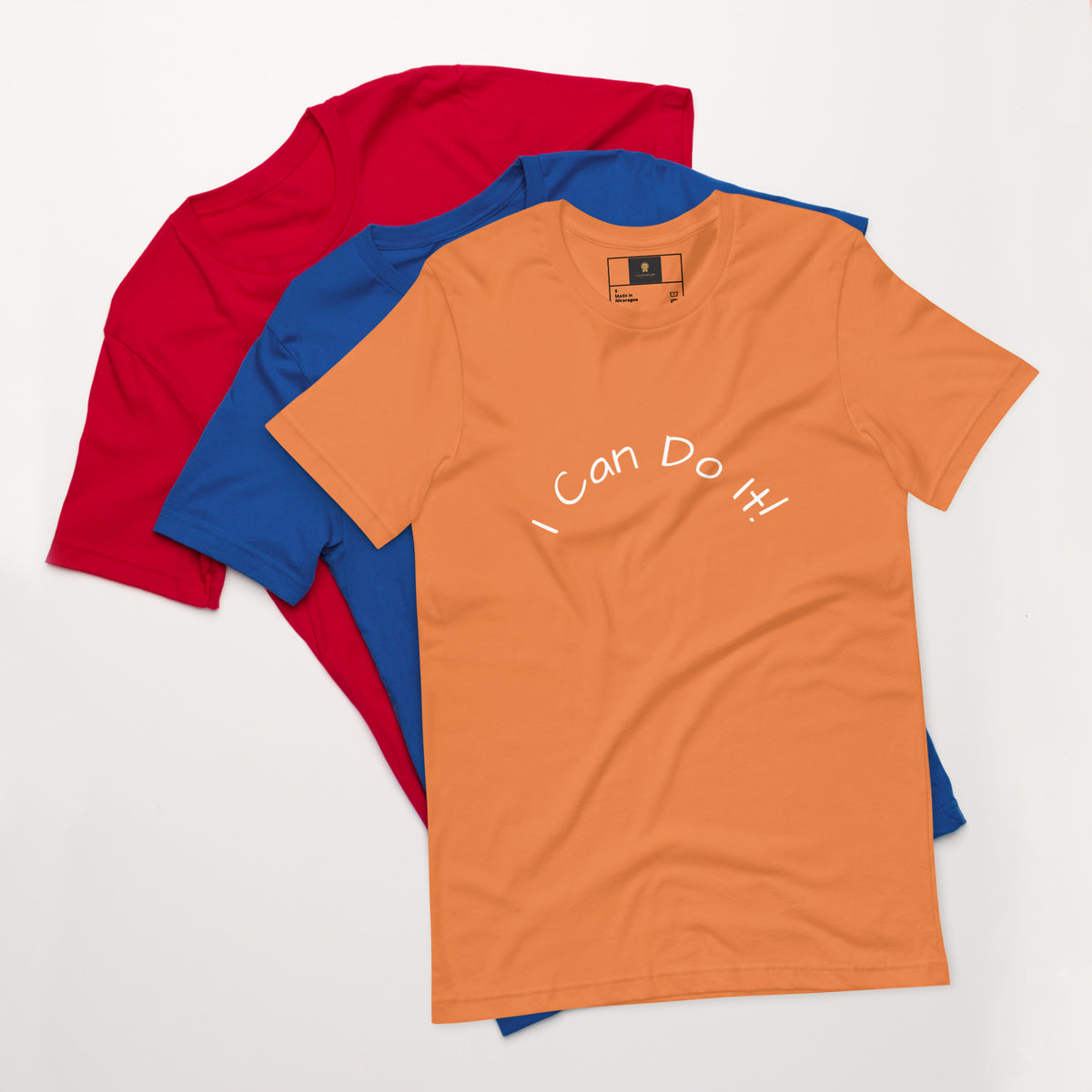 I Can Do It Unisex T-shirt in gray with red and blue shirts stacked in the background.