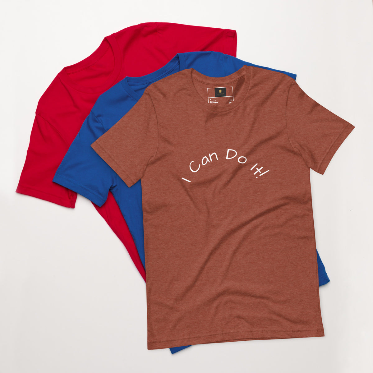I Can Do It Unisex T-shirt in gray with red and blue shirts stacked in the background.