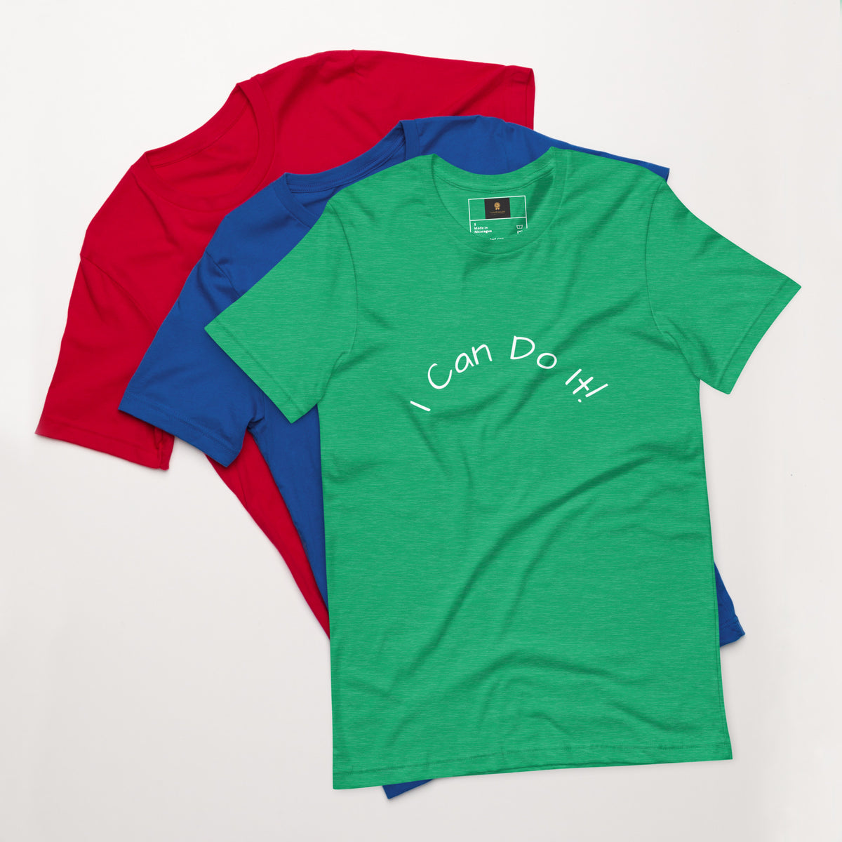 I Can Do It Unisex T-shirt in gray with red and blue shirts stacked in the background.