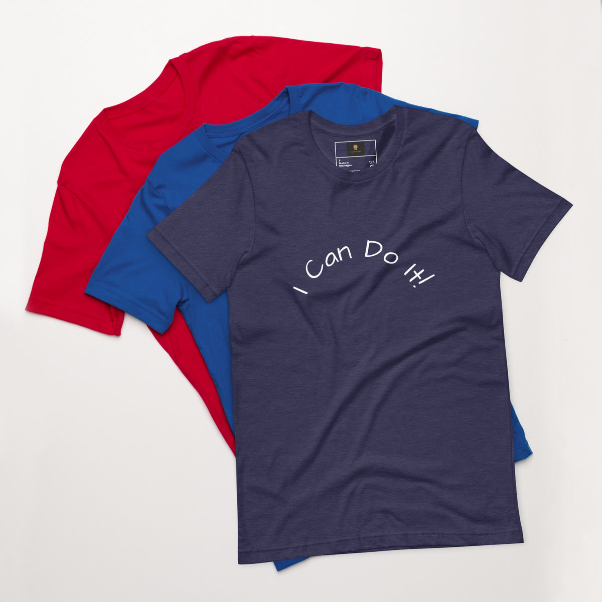 I Can Do It Unisex T-shirt in gray with red and blue shirts stacked in the background.