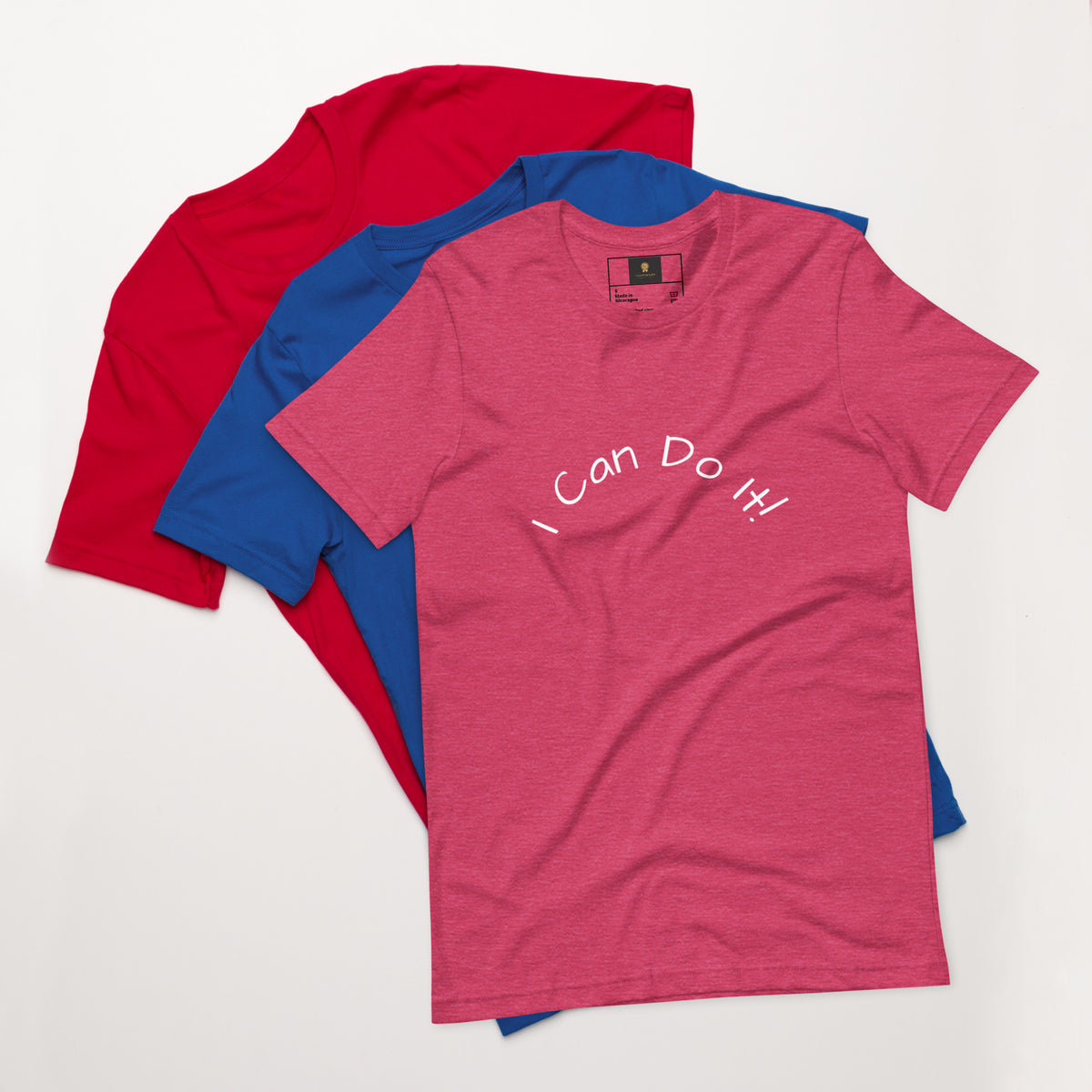 I Can Do It Unisex T-shirt in gray with red and blue shirts stacked in the background.