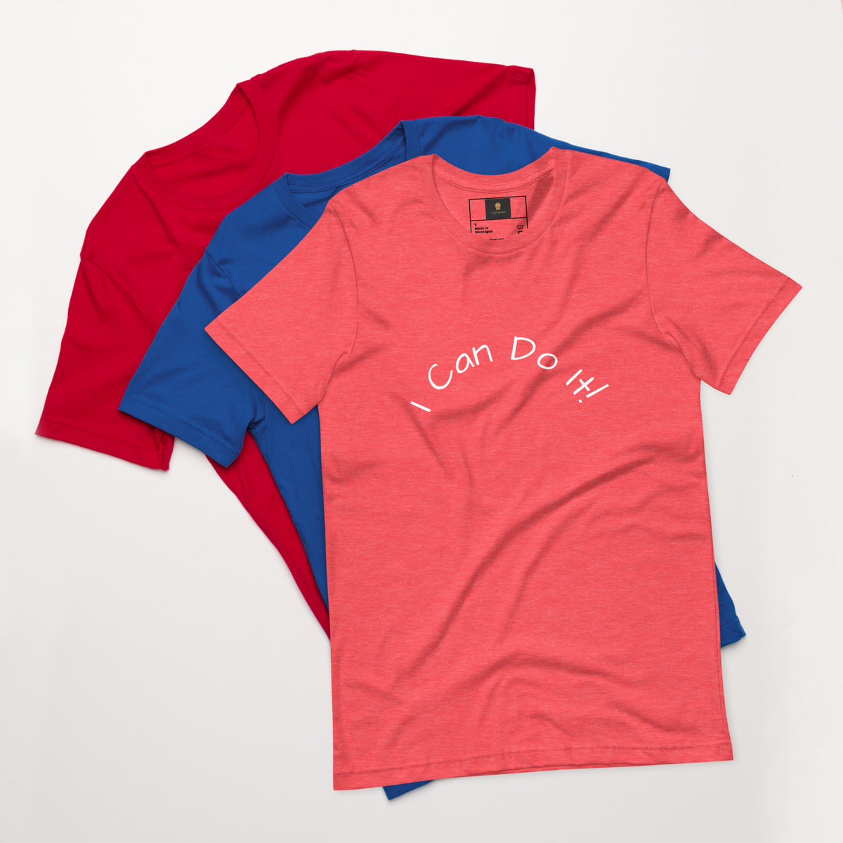 I Can Do It Unisex T-shirt in gray with red and blue shirts stacked in the background.