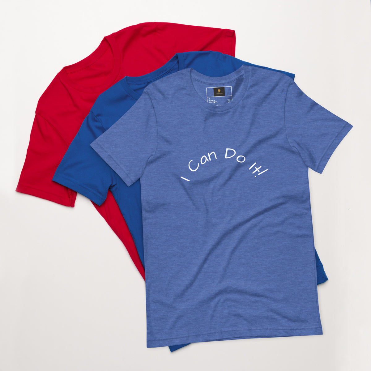 I Can Do It Unisex T-shirt in gray with red and blue shirts stacked in the background.