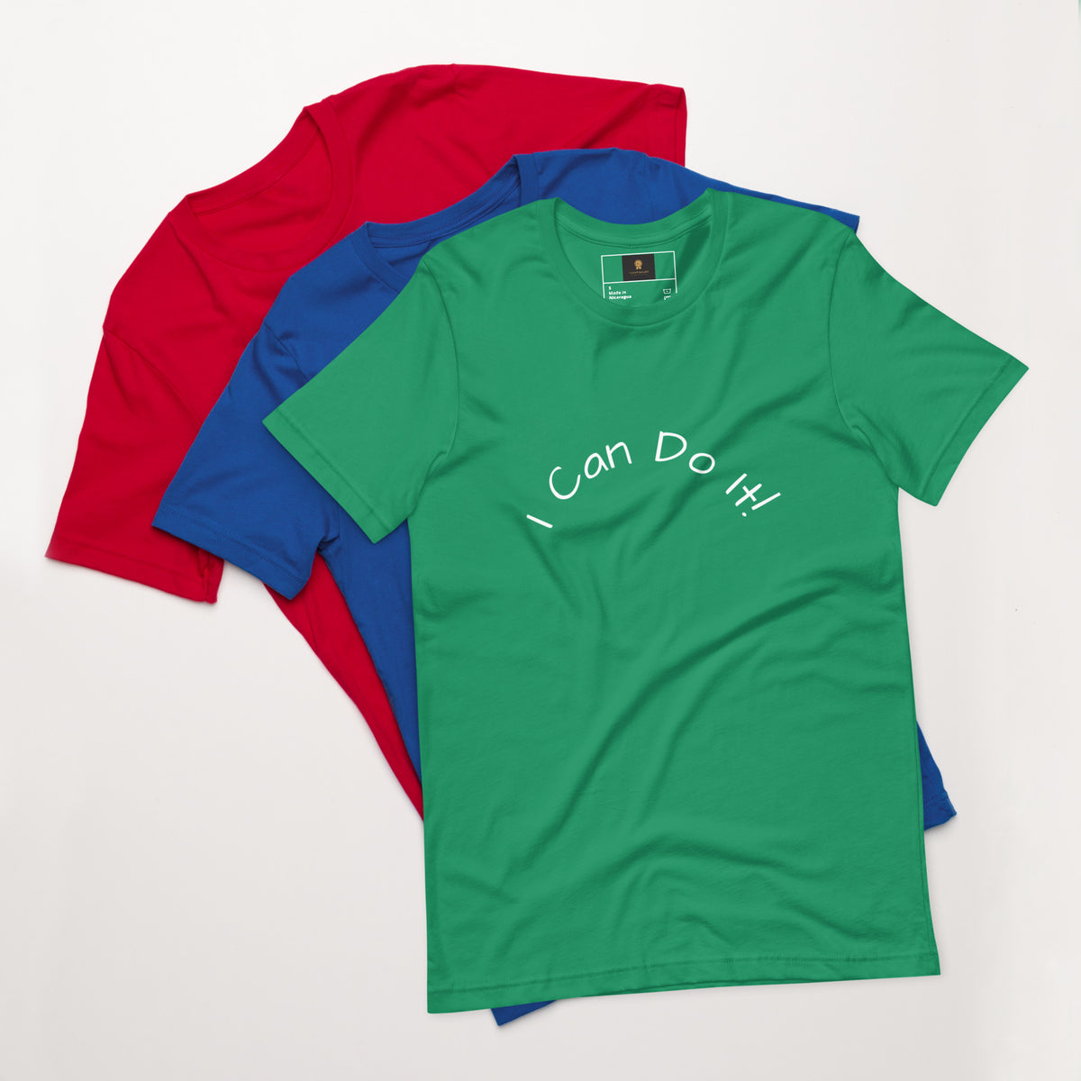 I Can Do It Unisex T-shirt in gray with red and blue shirts stacked in the background.
