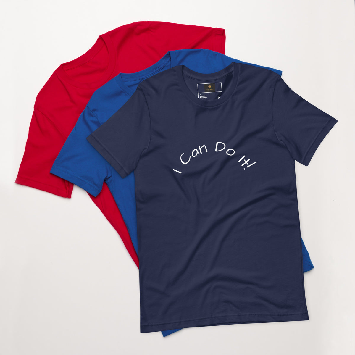 I Can Do It Unisex T-shirt in gray with red and blue shirts stacked in the background.