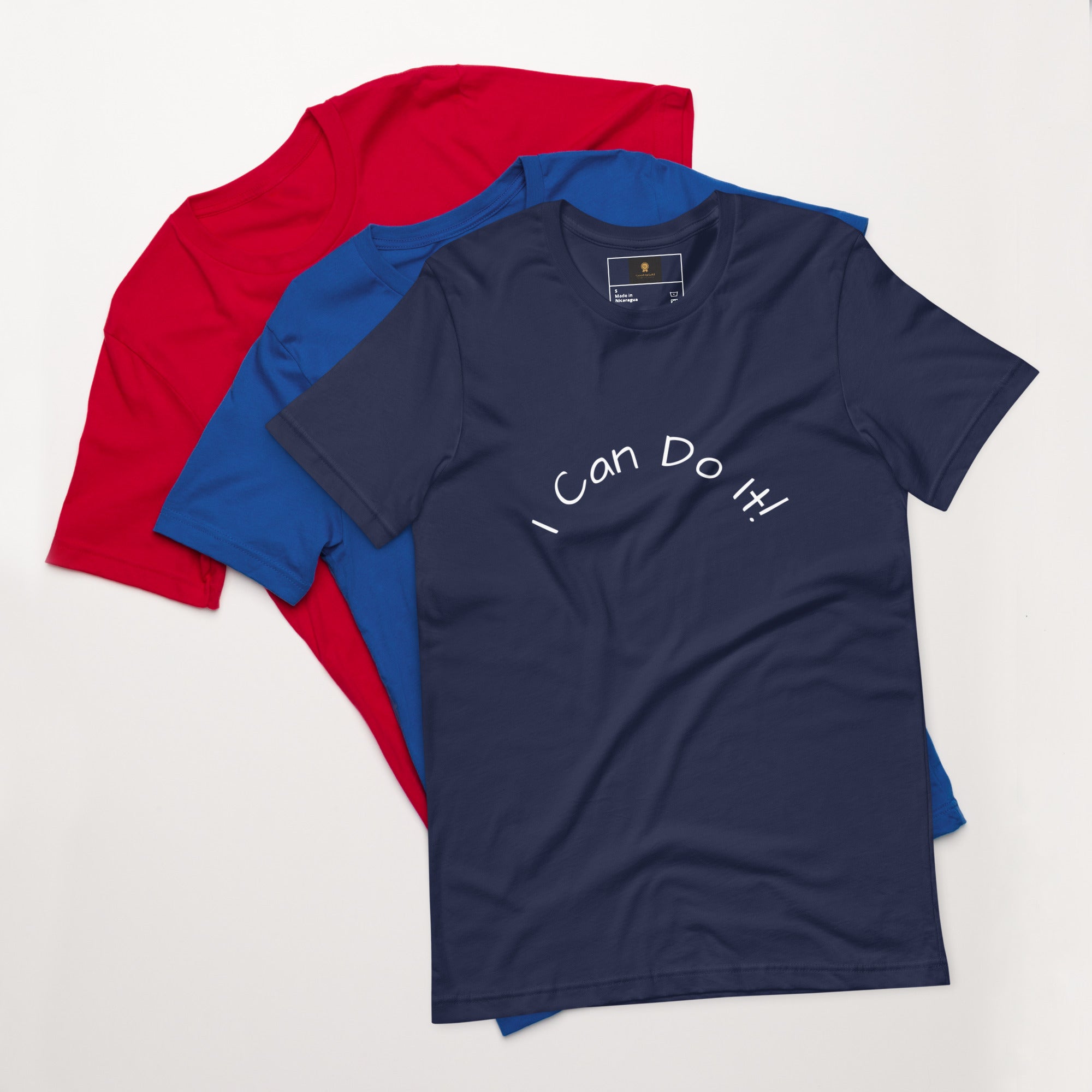 I Can Do It Unisex T-shirt in gray with red and blue shirts stacked in the background.
