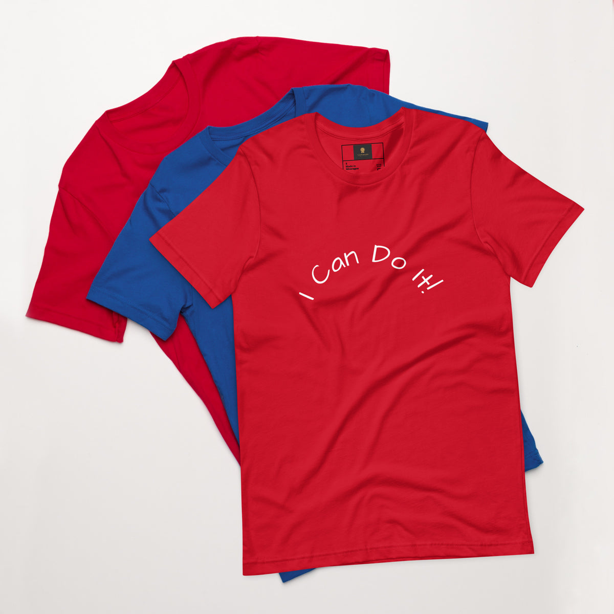I Can Do It Unisex T-shirt in gray with red and blue shirts stacked in the background.