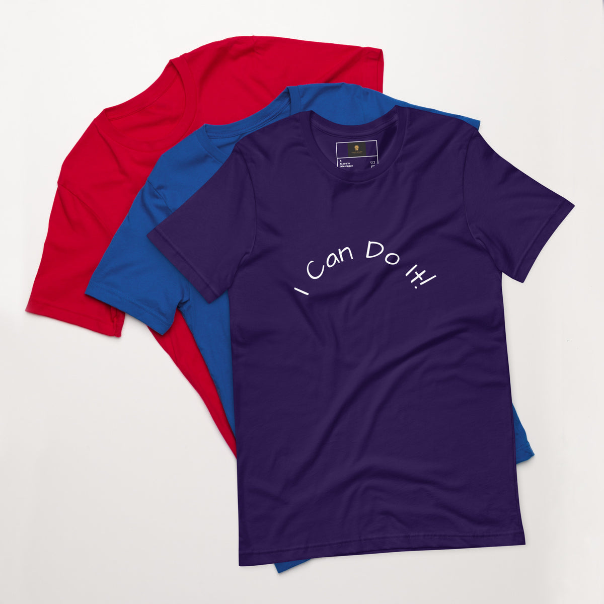 I Can Do It Unisex T-shirt in gray with red and blue shirts stacked in the background.