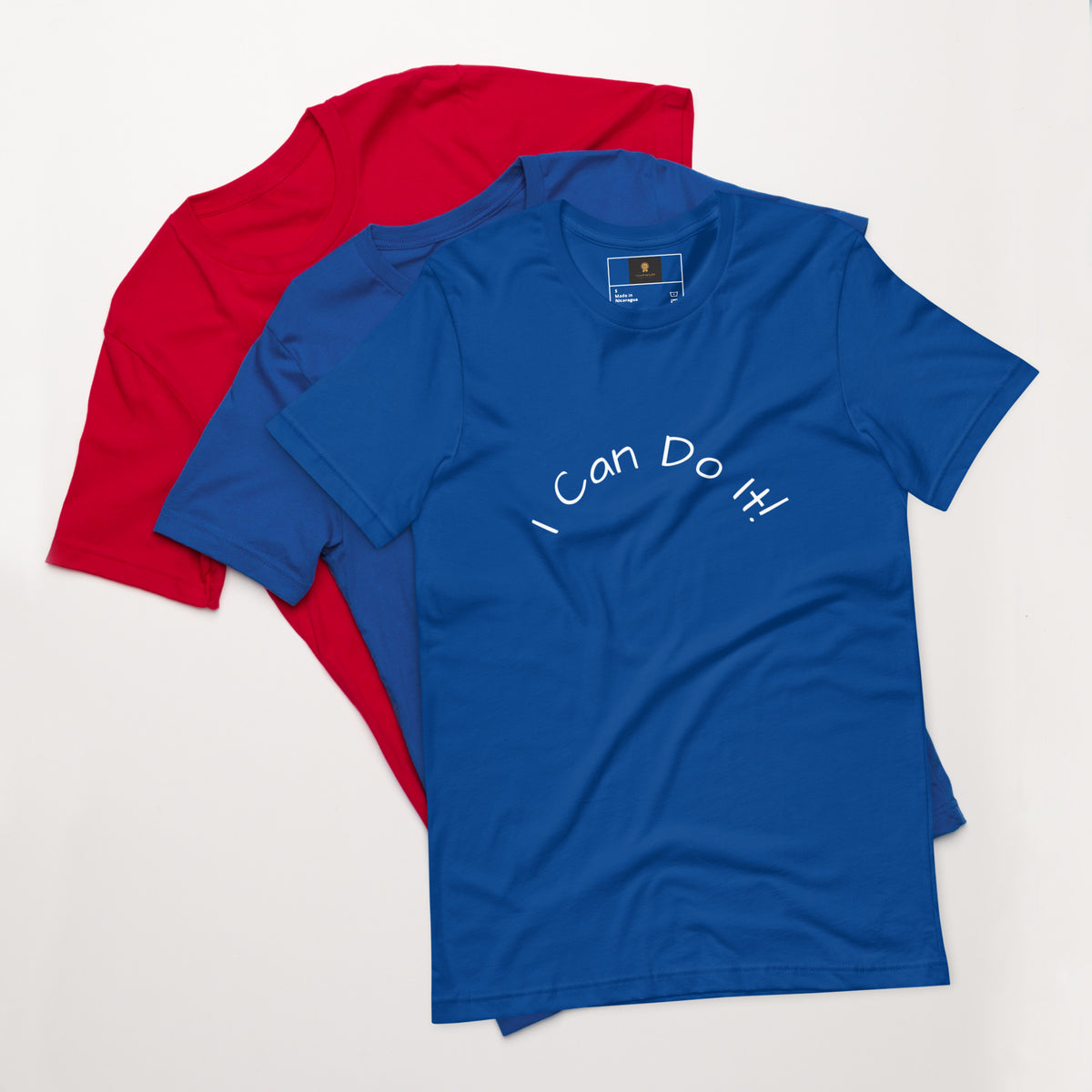 I Can Do It Unisex T-shirt in gray with red and blue shirts stacked in the background.